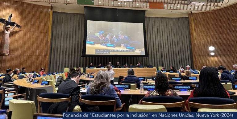 Fotografía. Vista posterior de una conferencia en las Naciones Unidas durante la ponencia 'Estudiantes por la inclusión' en 2024. Al fondo, siete moderadores frente a micrófonos. Sobre estos, las intervenciones de la audiencia se emiten en una gran pantalla con traducción al inglés.