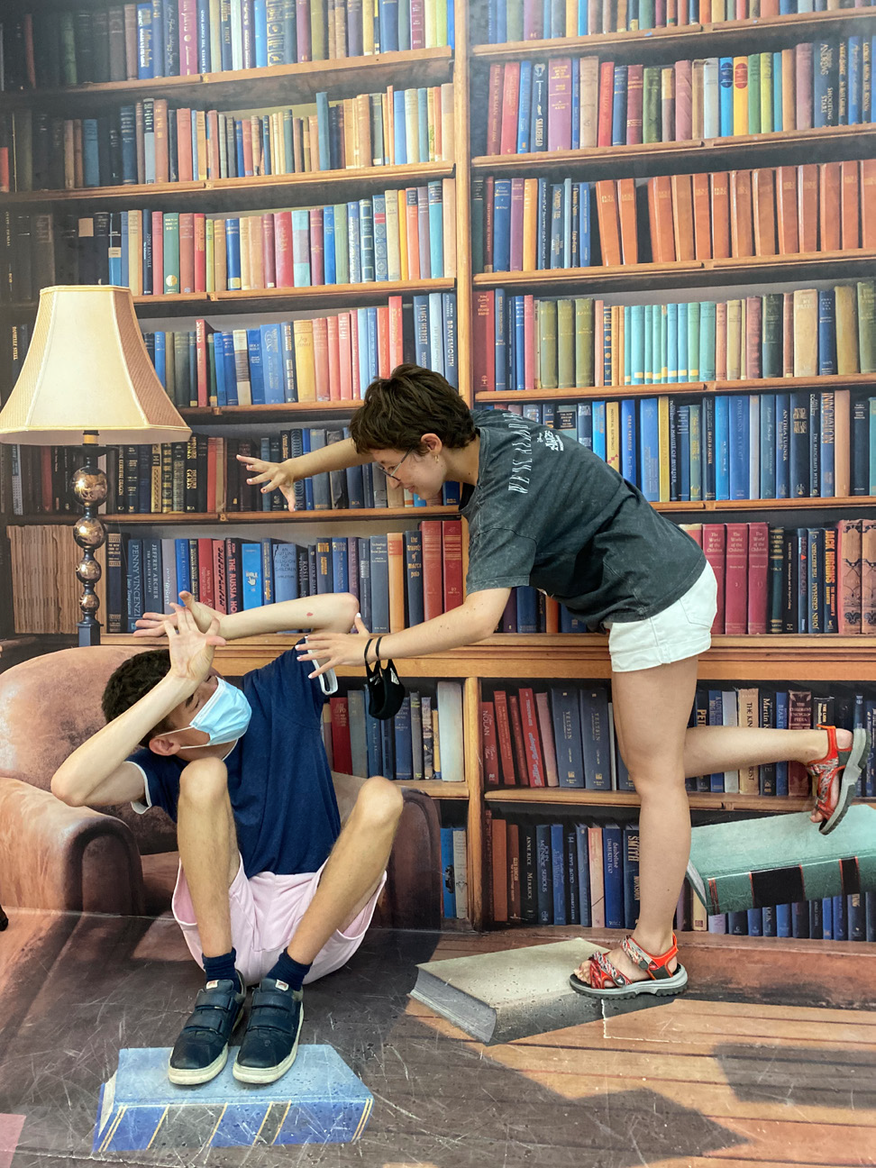 Fotografía, collage. Dos jóvenes del grupo 'Estudiantes por la Inclusión' frente a una biblioteca pintada en la pared con numerosos libros.