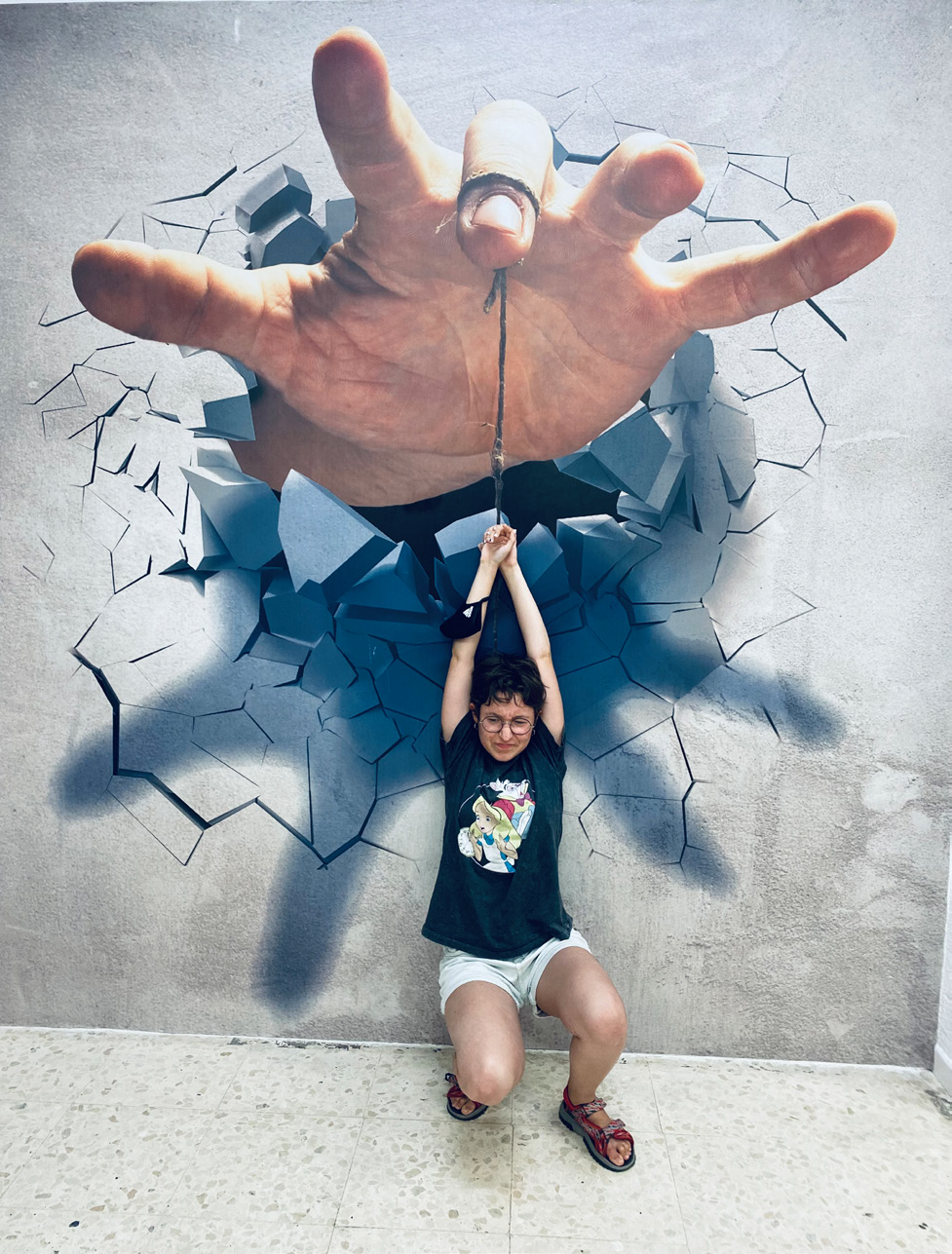 Fotografía, collage. Una joven del grupo 'Estudiantes por la Inclusión' parece estar atada con una cuerda que sostiene una gran mano pintada en la pared.