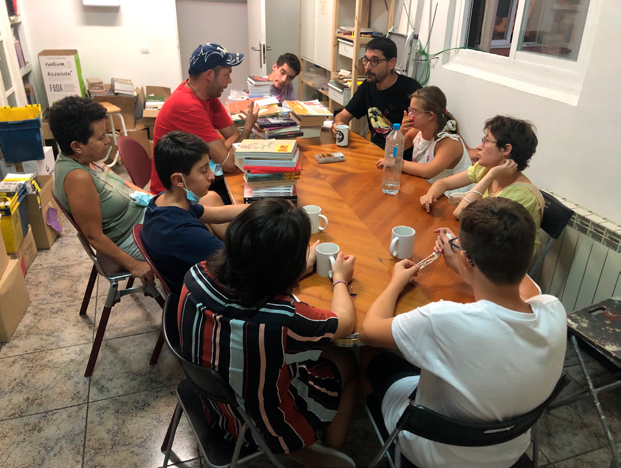 Fotografía. Un grupo de personas reunidas alrededor de una mesa en una sala repleta de libros y documentos. 