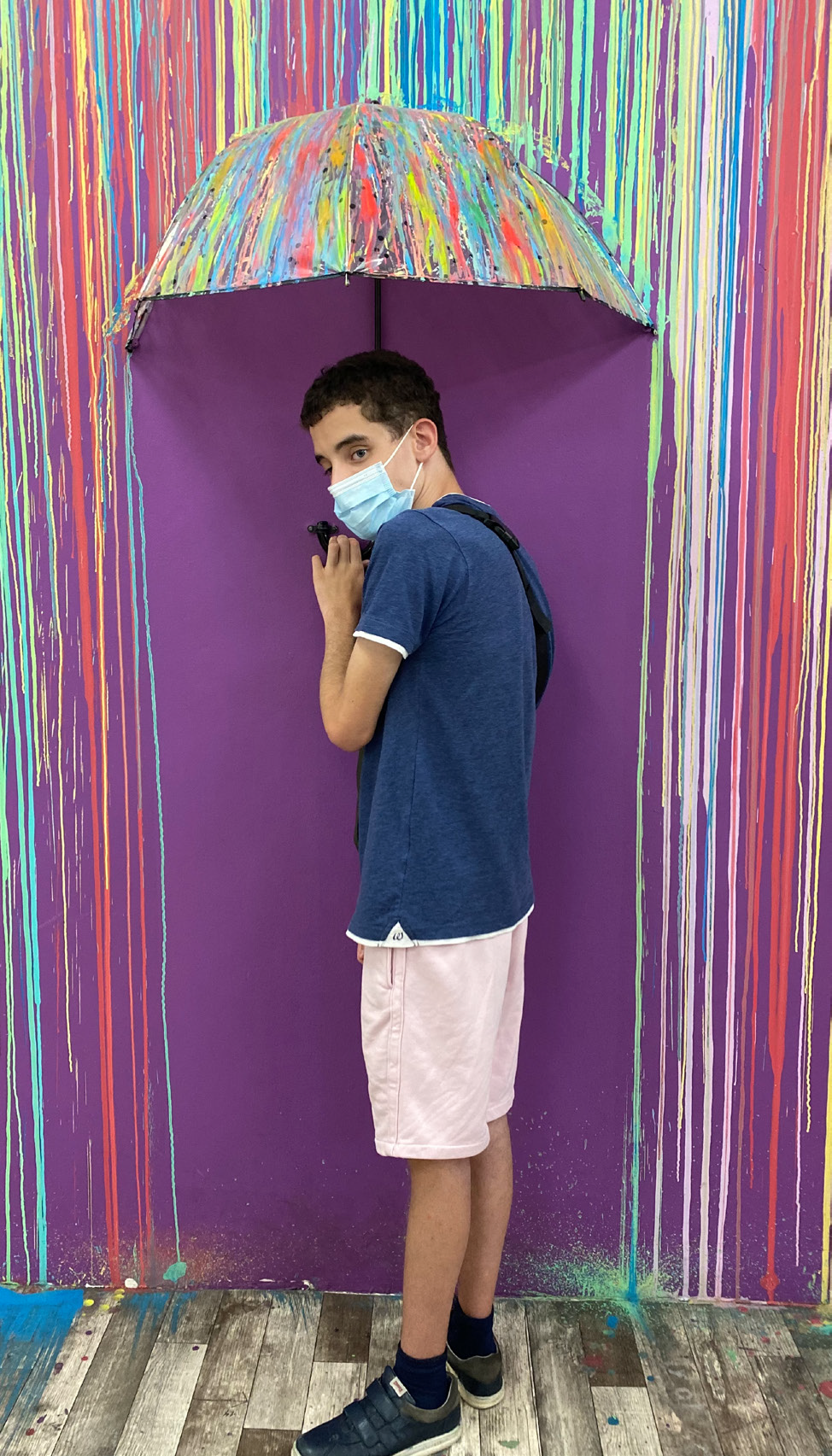 Fotografía, collage. Vista frontal de un joven bajo un paraguas, protegiéndose de una lluvia de colores.