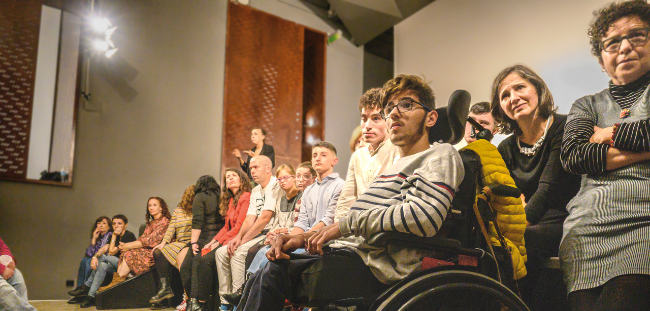 Instantánea del estreno del documental «Quererla es Crearla», en el Museo Reina Sofía. Se observa una vista lateral de un grupo de personas, con y sin discapacidad, atentas a la proyección del documental en un auditorio.