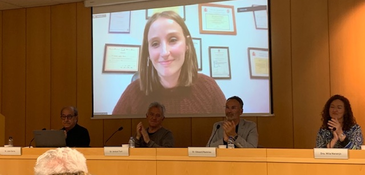 Fotografía del acto de entrega, con el Jurado del premio tras una mesa. Detrás de ellos, proyectada en una pantalla y en grande, Sonia, la premiada, sonríe.