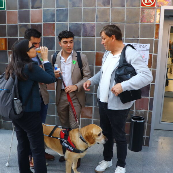 Fotografía. 4 personas conversan en el hall del Ministerio. Una de ellas lleva un perro guía, que está entre todas ellas.