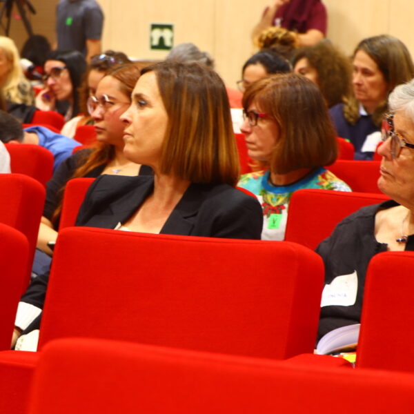 Fotografía. Varias personas escuchan sentadas en el salón de actos durante una asamblea.