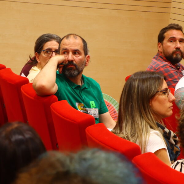 Fotografía. Debate en el salón de actos del ministerio, una sala amplia con buena iluminación y asientos plegables con tapicería de tela roja. Hay mucha gente que escuchando a alguien fuera del foco.