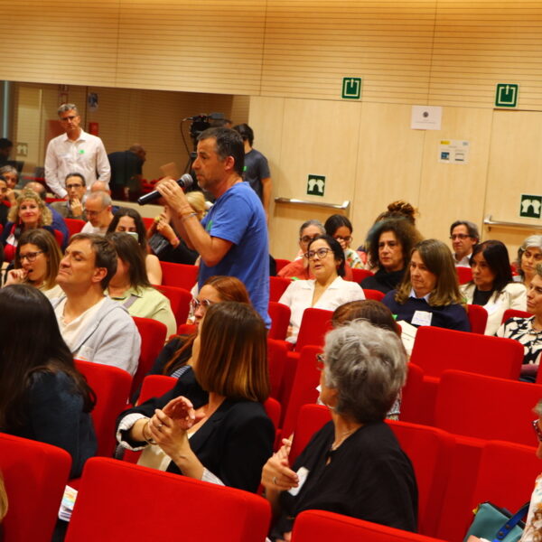 Fotografía. Debate en el salón de actos del ministerio, una sala amplia con buena iluminación y asientos plegables con tapicería de tela roja. Hay mucha gente y una persona toma la palabra.