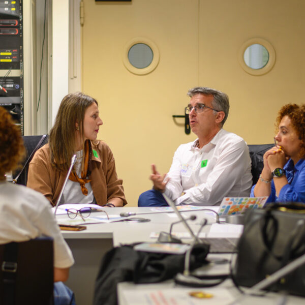 Fotografía. Participantes en una mesa de reuniones debaten y toman notas.