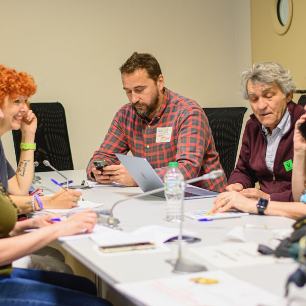 Fotografía. Participantes en una mesa de reuniones debaten y toman notas.