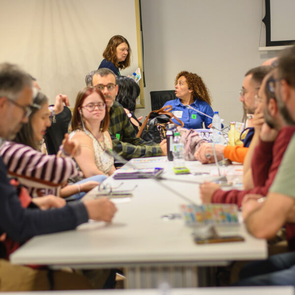 Fotografía. Participantes en una mesa de reuniones debaten y toman notas.