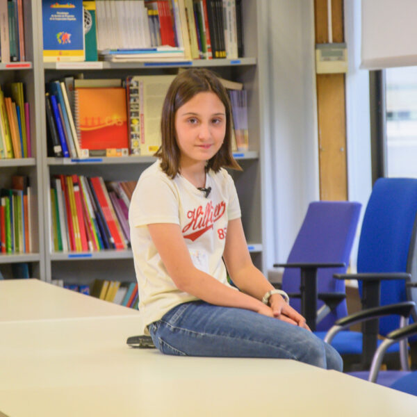 Fotografía. Una estudiante posa sentada en el borde de una mesa.