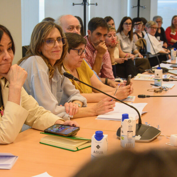 Fotografía. Participantes de un taller, en una mesa de reuniones, debaten, escuchan y toman notas.