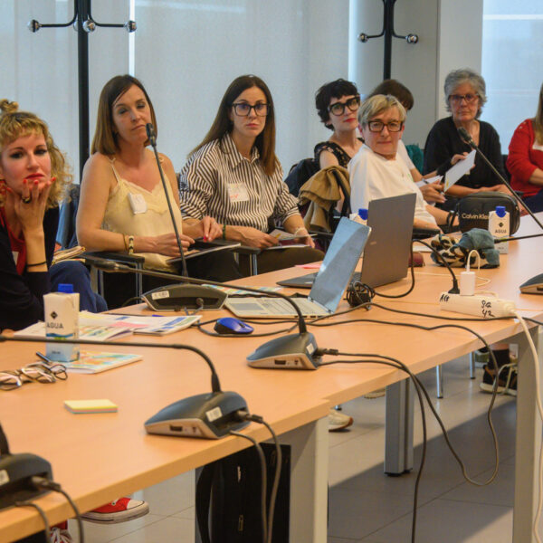 Fotografía. Participantes de un taller, en una mesa de reuniones, debaten, escuchan y toman notas.
