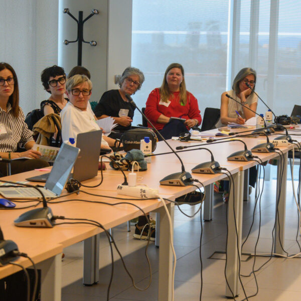Fotografía. Participantes de un taller, en una mesa de reuniones, debaten, escuchan y toman notas.