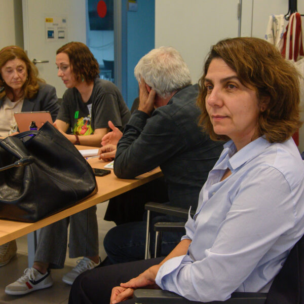 Fotografía. Participantes de un taller, en una mesa de reuniones, debaten, escuchan y toman notas.