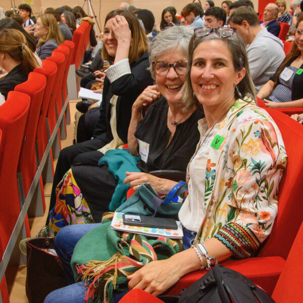 Fotografía. Dos mujeres, en el salón de actos, sentadas, sonríen a la cámara.