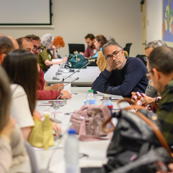 Fotografía. Participantes en una mesa de reuniones debaten y toman notas.