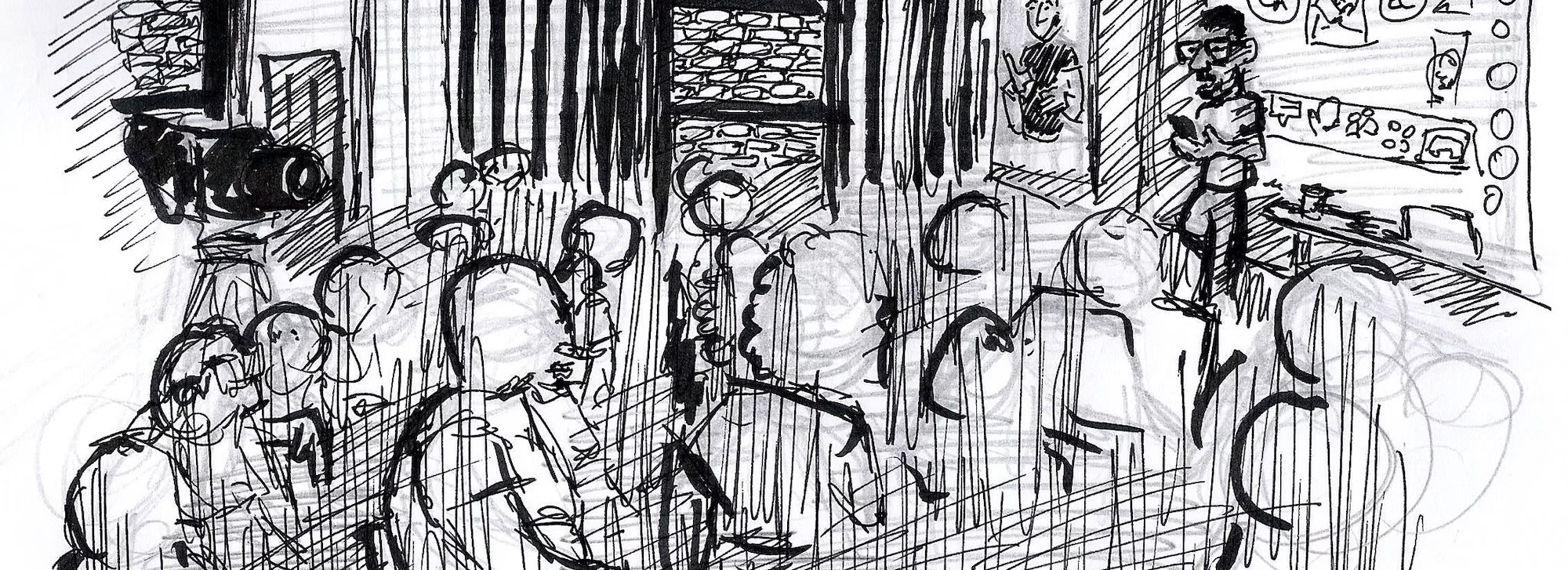 Dibujo a rotulador negro, durante un workshop de Quererla es Crearla. La escena muestra un grupo de personas sentadas escuchando a alguien con barba y gafas, que está de pié frente a todas ellas y delante de una mesa y una pantalla. Al fondo se ve una persona haciendo la interpretación en lengua de signos.